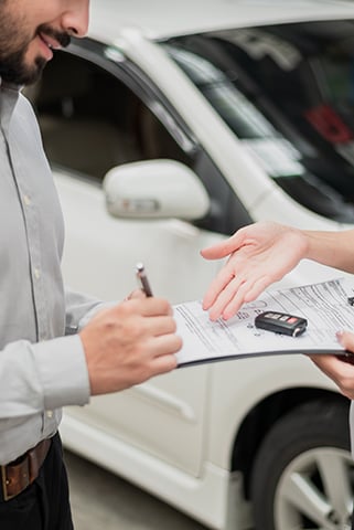 someone signing paperwork in front of a car