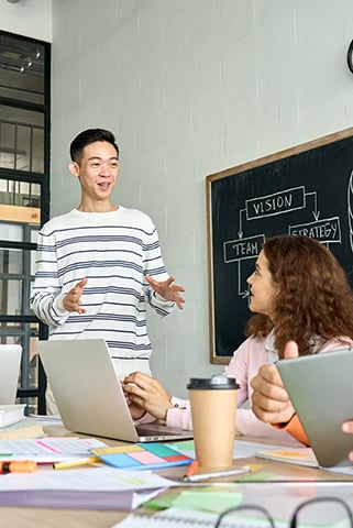 a young man standing and speaking in front of a blackboard