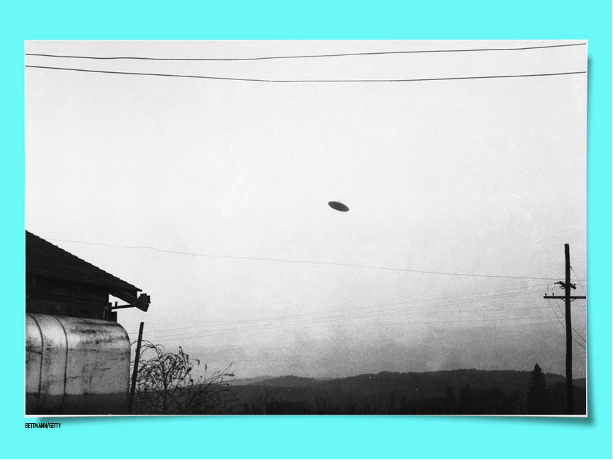 Black and white photo of a black dot in the sky above a phone line and house