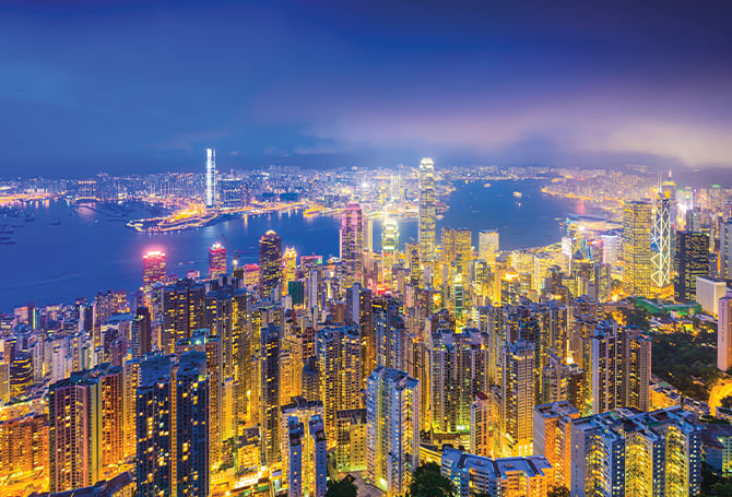 An aerial view of the brightly lit skyscrapers and buildings of a city lighting the night sky