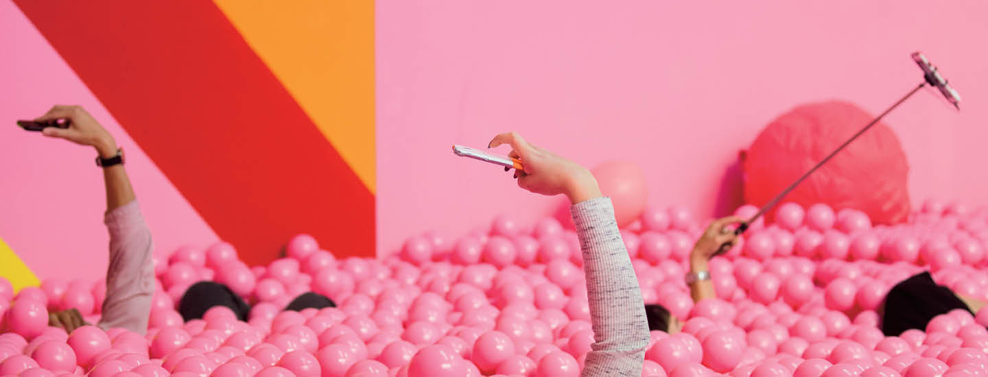 Hands holding phones sticking out of a pink ball pit 