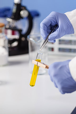Gloved hands holding a test tube with yellow liquid inside
