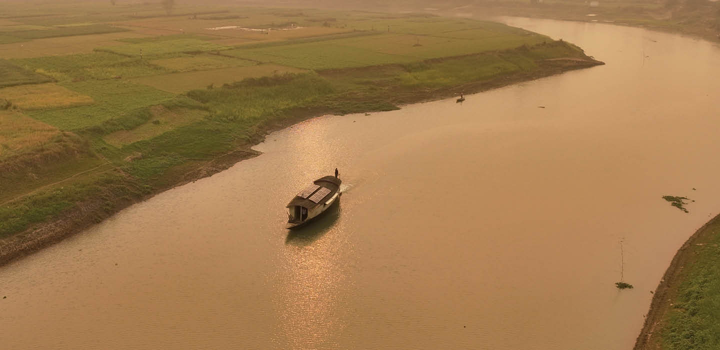 A small river boat with solar panels travels along a winding river beside farmland