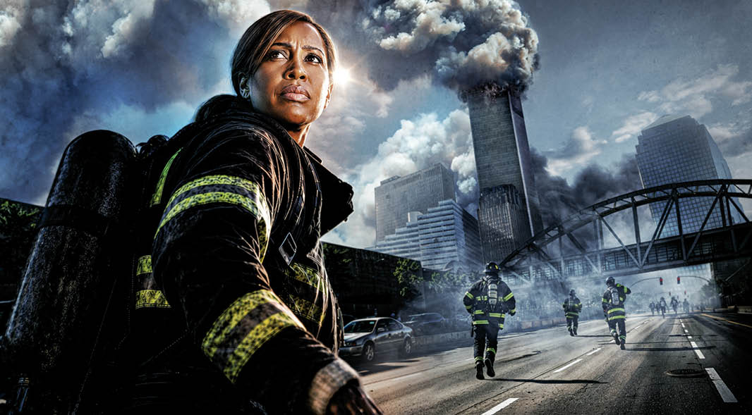 A firefighter stands in the foreground as others run toward a smoke-filled city skyline