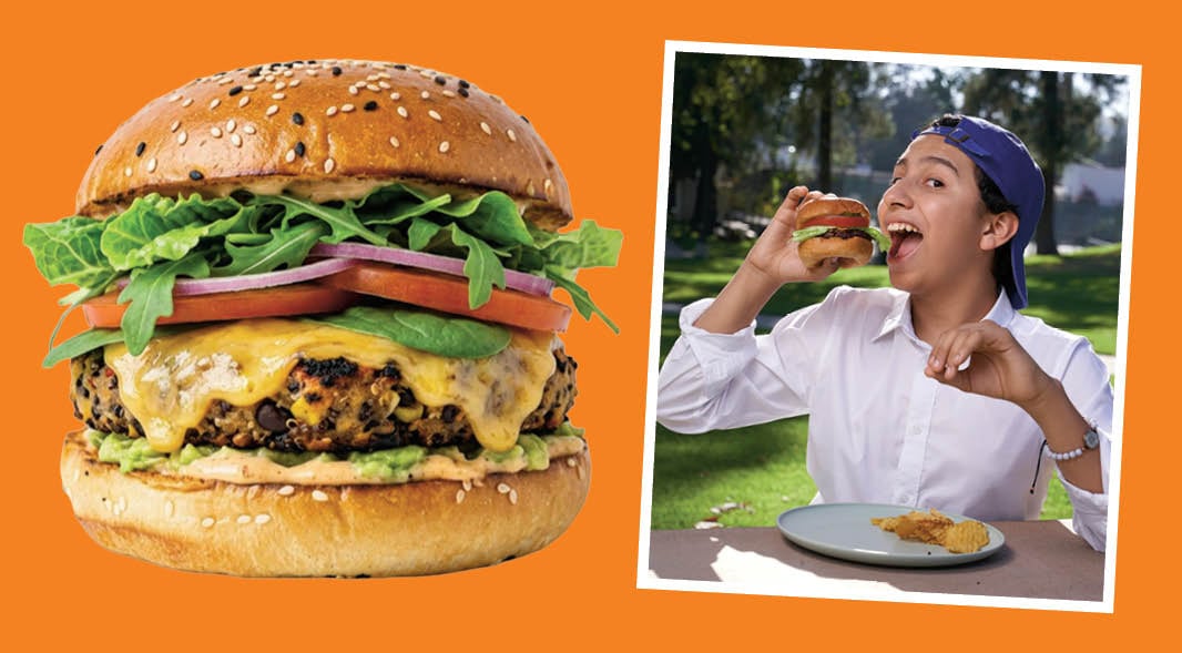A large burger with toppings next to a teen who eats a small burger at an outdoor table